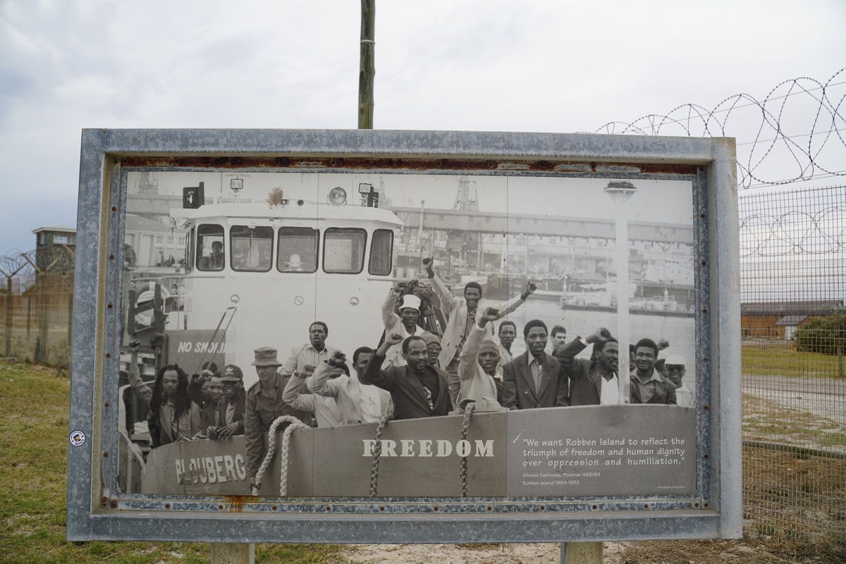 Ein Foto auf einem Schild zeigt Gefangene auf einem Boot, die zurück aufs Festland entlassen wurden