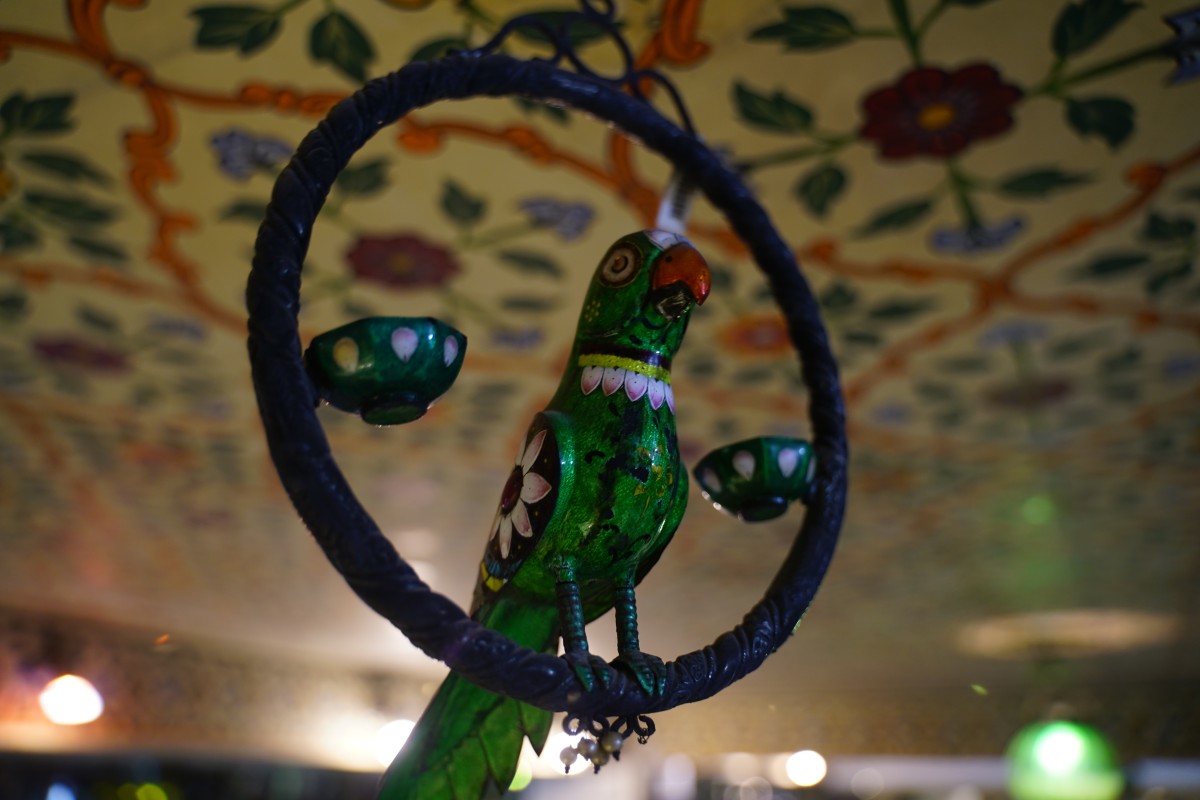 Eine grüne Papageienfigur in einem blauen Ring hängt an der Decke