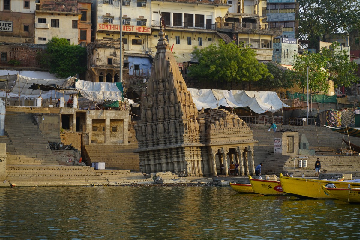 Sehr schiefes Gebäude (Ratneshwar-Mahadev-Tempel), das halb im Fluss steht und in dem trotzdem Menschen sitzen