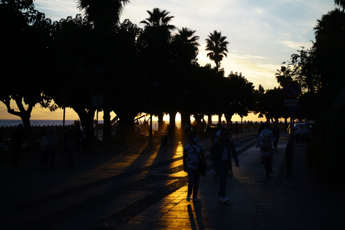 Leute in Alghero beobachten den Sonnenuntergang in Cafés an der Küste