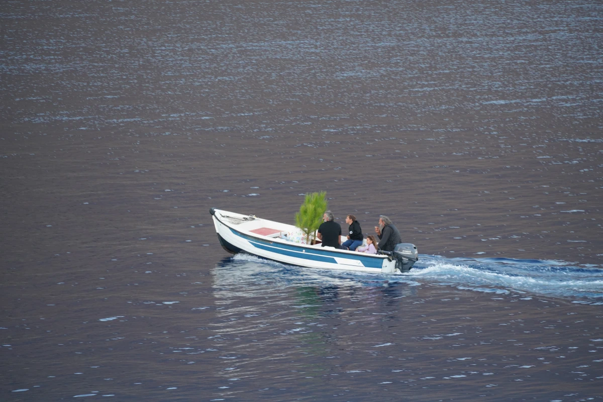 Eine Familie transportiert in Loutro auf Kreta zwei kleine Pinien in einem einfachen Boot