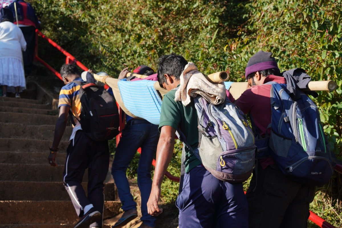 Vier Männer tragen jemanden auf einer Trage hoch zum Adam’s Peak